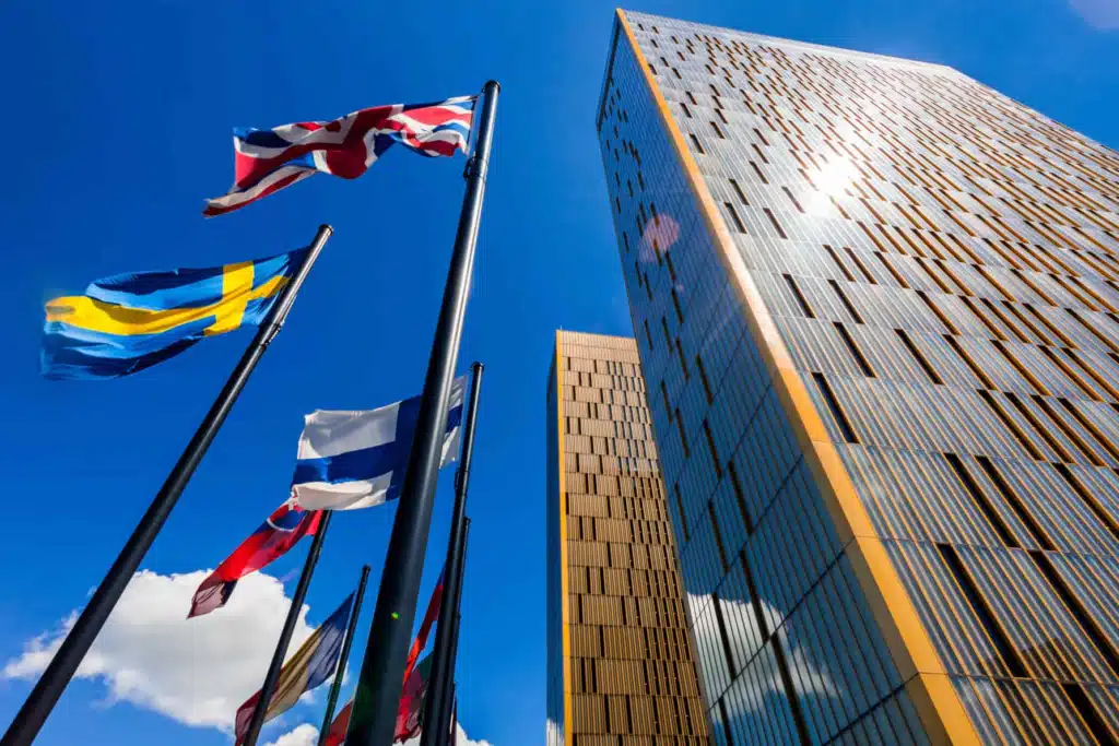Modern skyscrapers of the European Court of Justice in Luxembourg with waving EU member state flags against a blue sky.