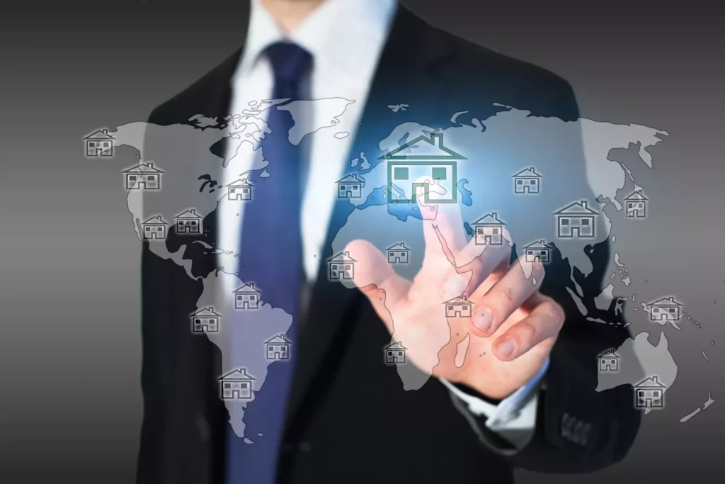 Businessman in suit touches virtual house symbol on world map - symbolic image for international property investment and asset management.