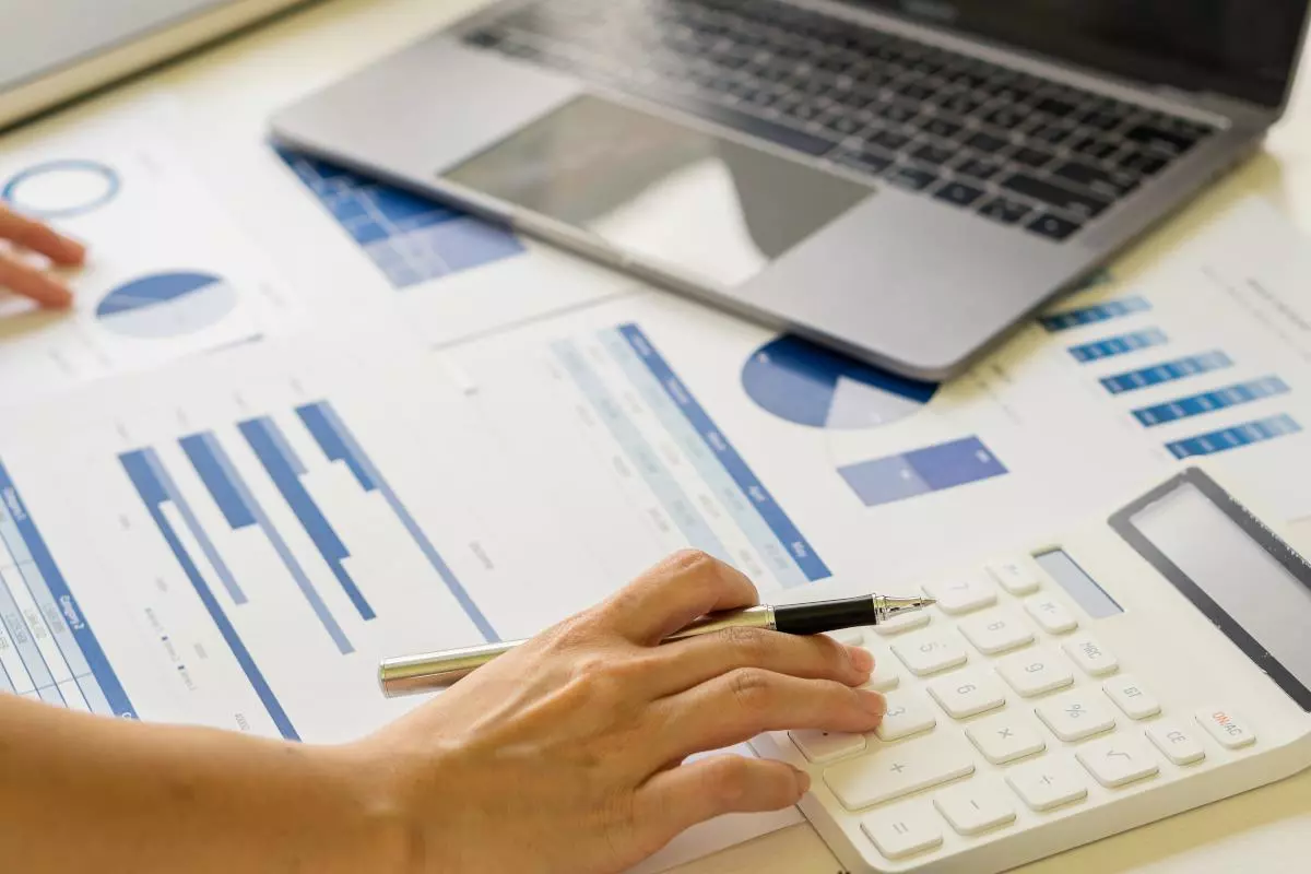 Person works with calculator on financial documents with laptop in the background